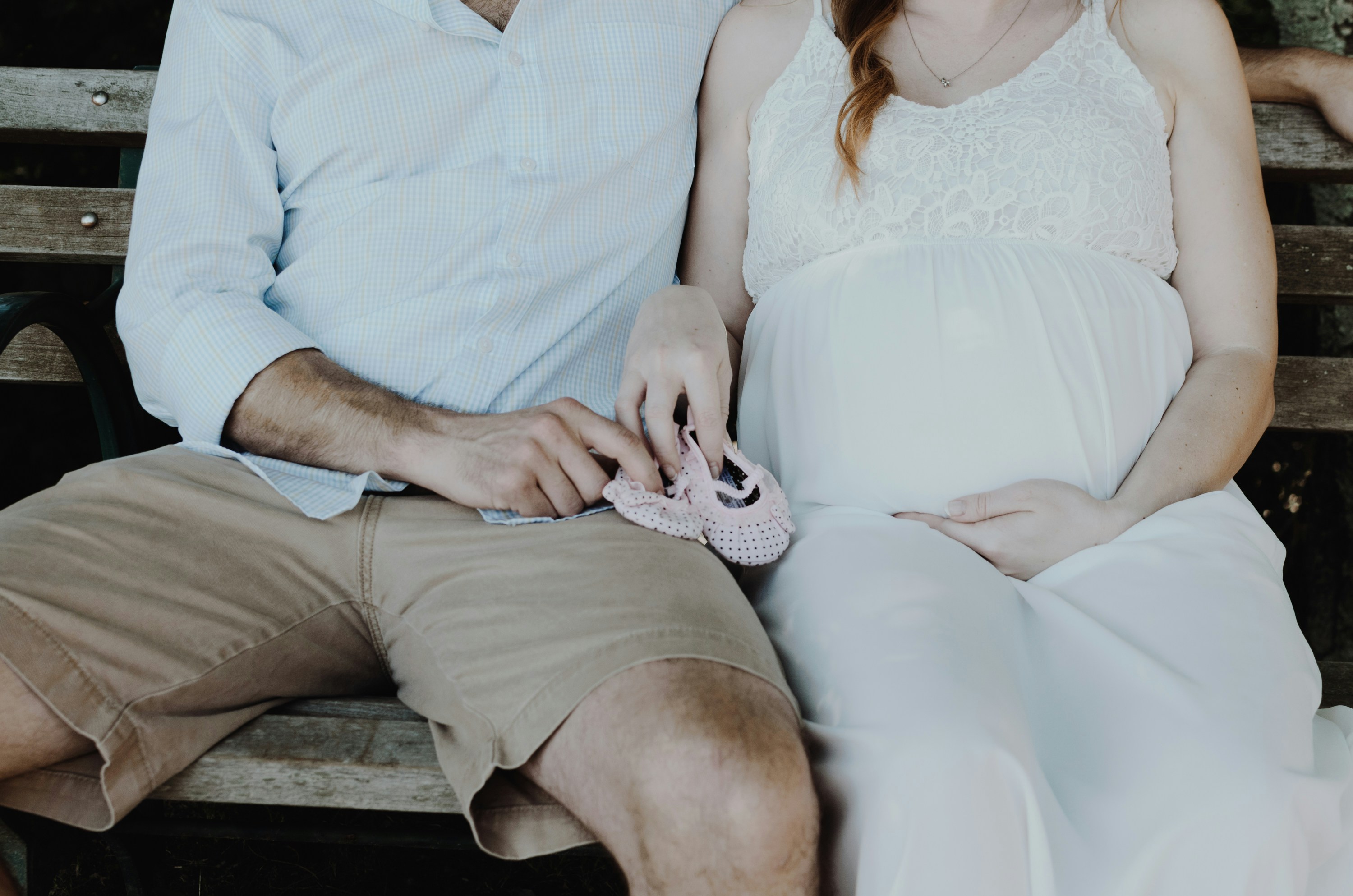 A man and woman on sitting on a bench holding baby slippers.